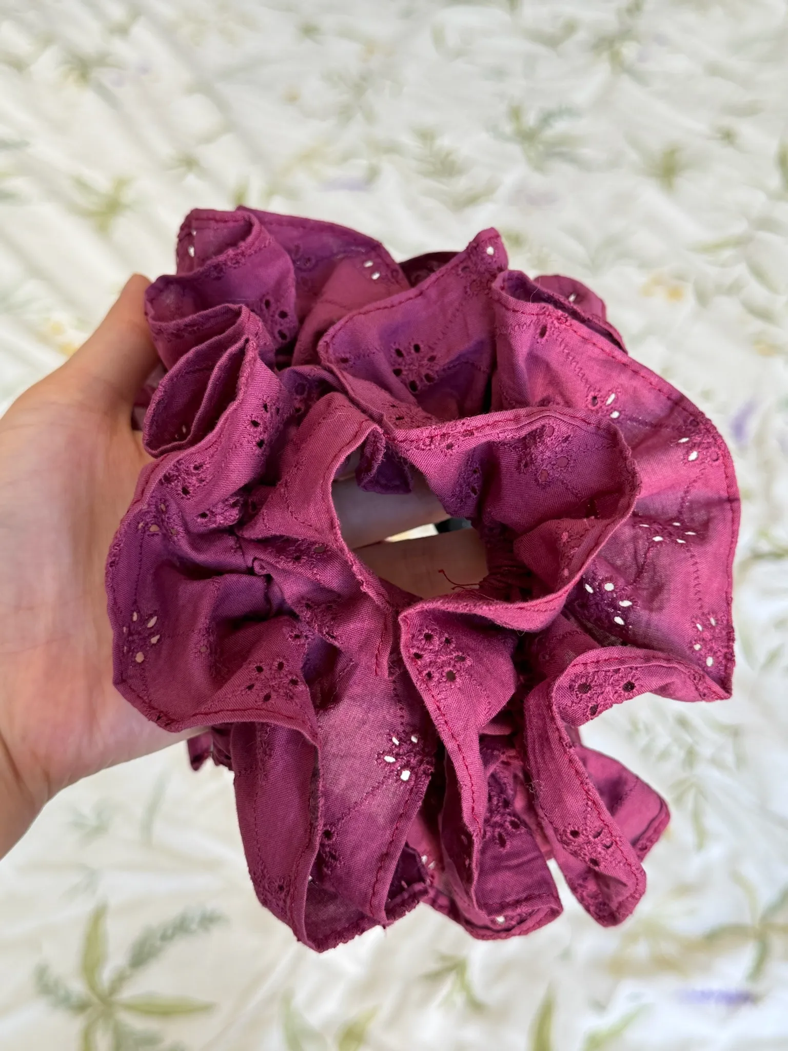 A hand holds a berry-coloured HemHugger, showing ruffled fabric with small floral cut-out details.