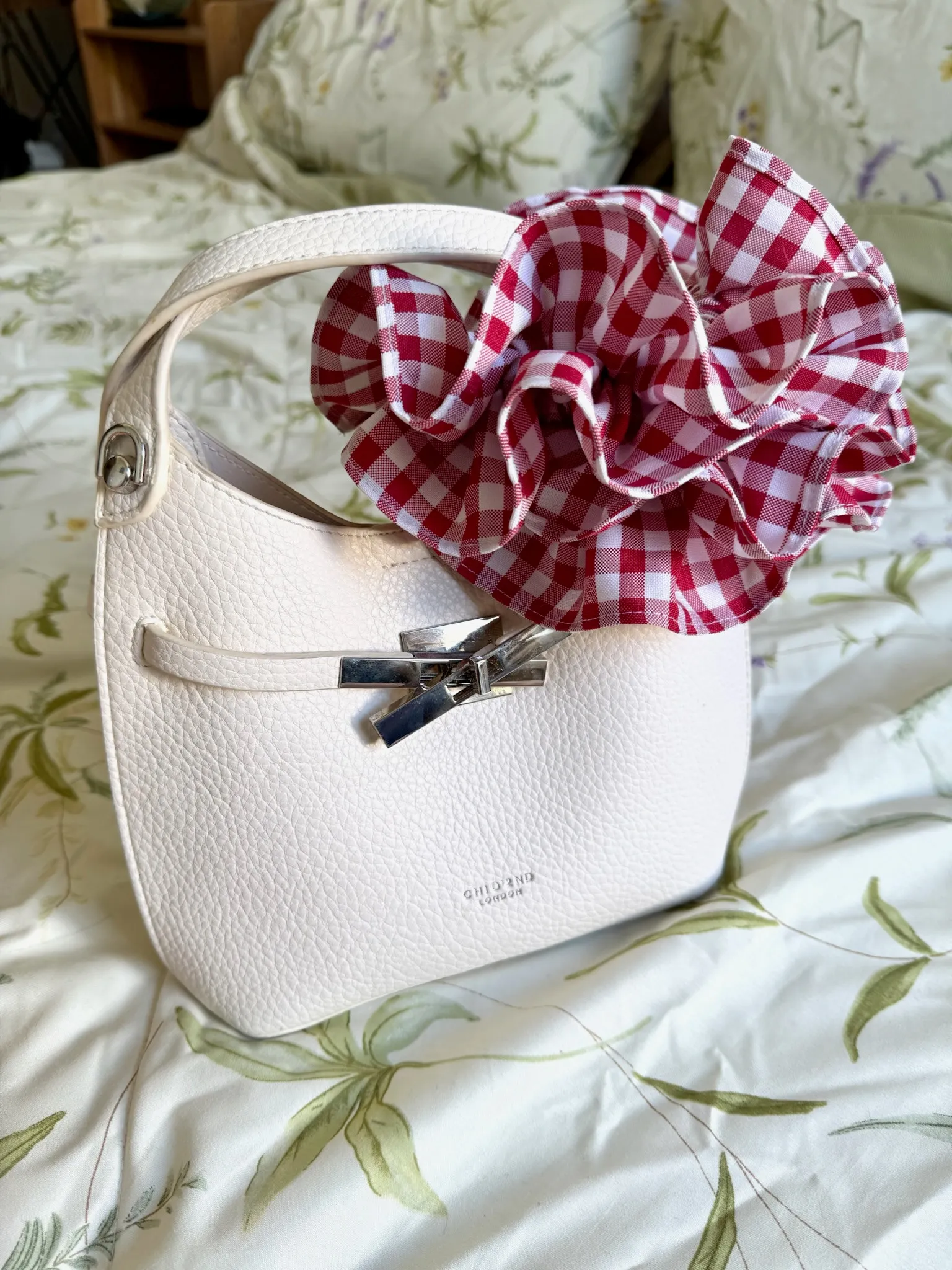 A red-and-white gingham HemHugger clipped around the handle of a white handbag, with its frills forming a decorative flourish.