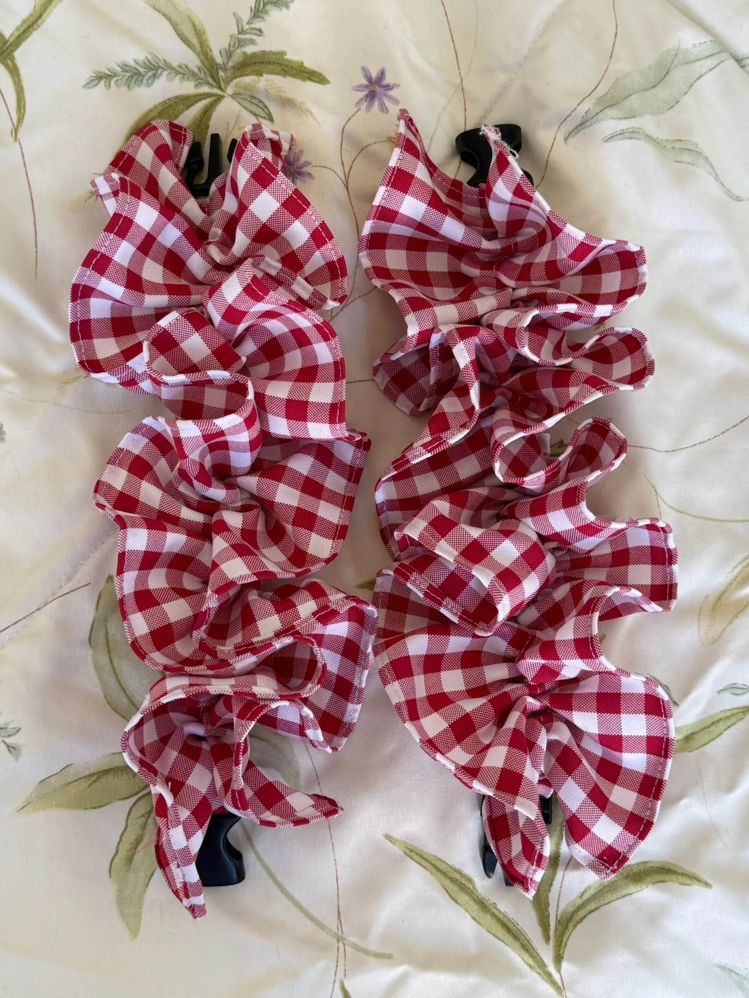 Two red-and-white gingham HemHuggers laid open on floral fabric, showing the gathered frills and black clips at each end.
