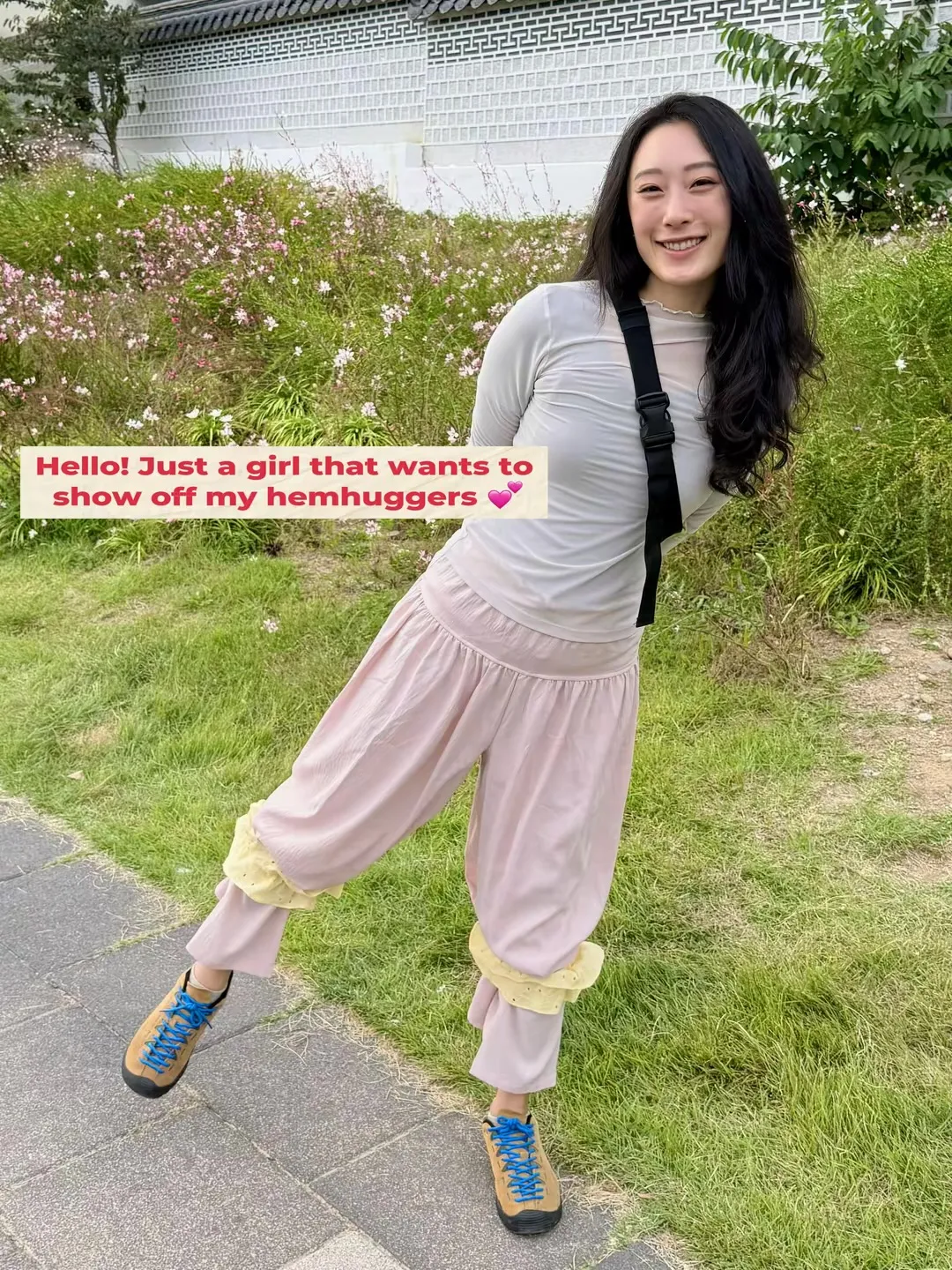 A woman outdoors wearing pink wide-leg trousers gathered below the knees with yellow, frilled HemHuggers. The photo reads: “Hello! Just a girl that wants to show off my hemhuggers.”